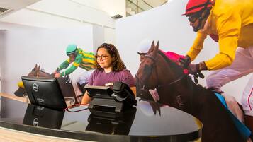 Una mujer frente a un escritorio con una computadora portátil y un monitor, en una habitación con un cartel grande de jinetes a caballo.