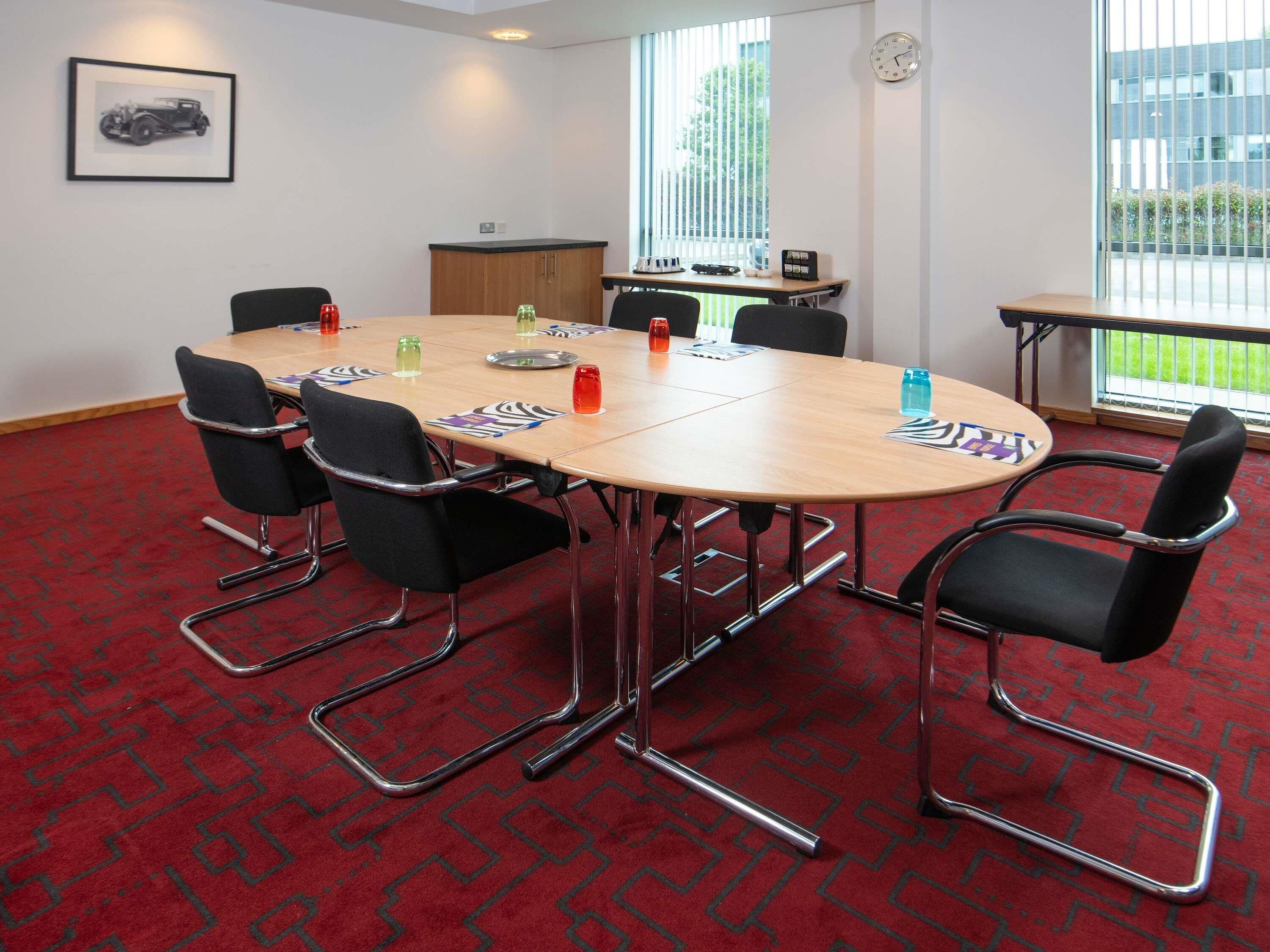 A conference room with a round table, black chairs, and a red patterned carpet.