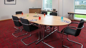 A conference room with a round table, black chairs, and a red patterned carpet.