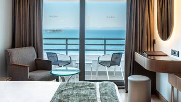 Habitación de hotel con cama, escritorio, silla, una mesita y vista al mar.