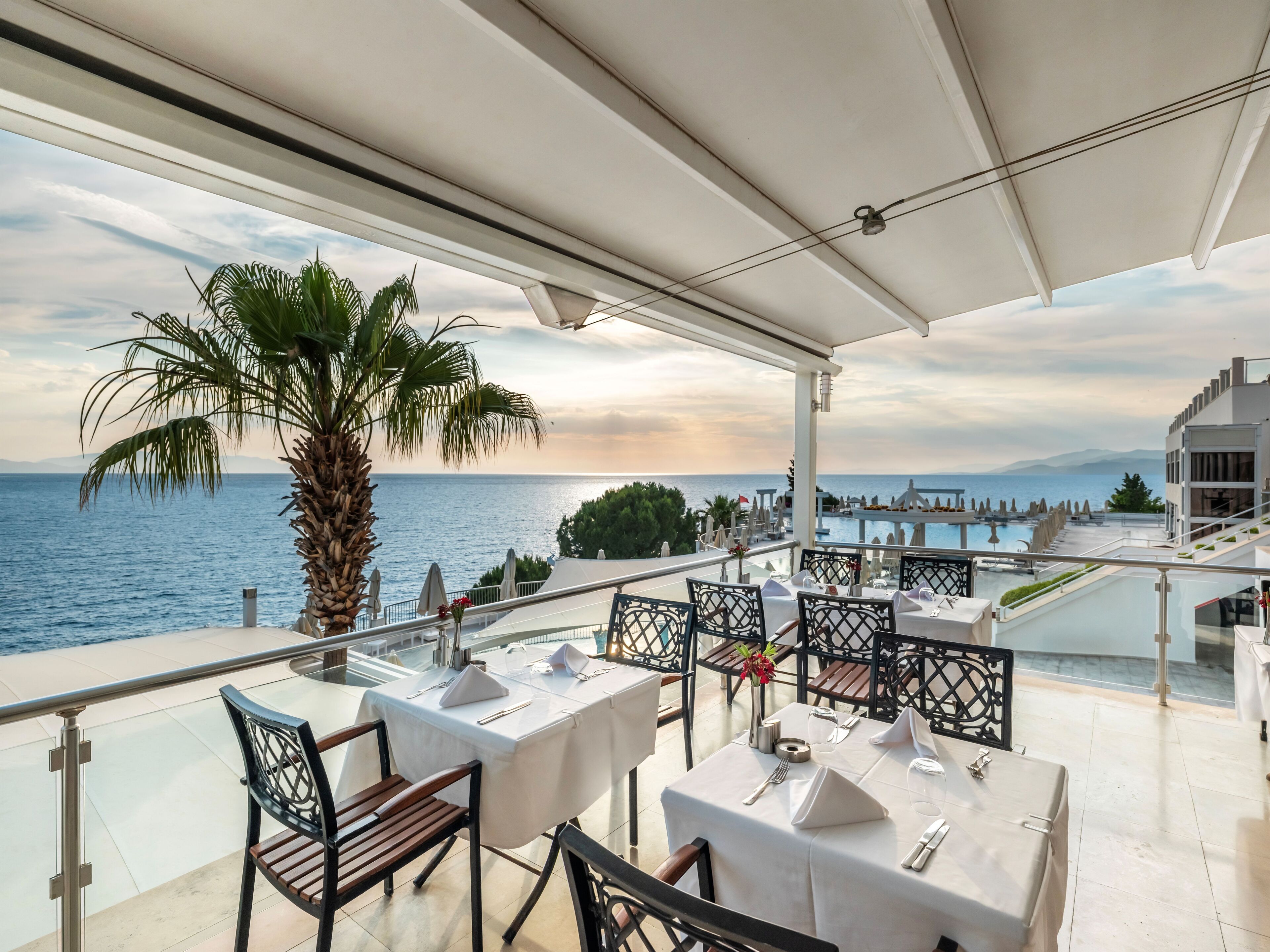 A terrace with tables set for dining, overlooking a body of water and mountains.