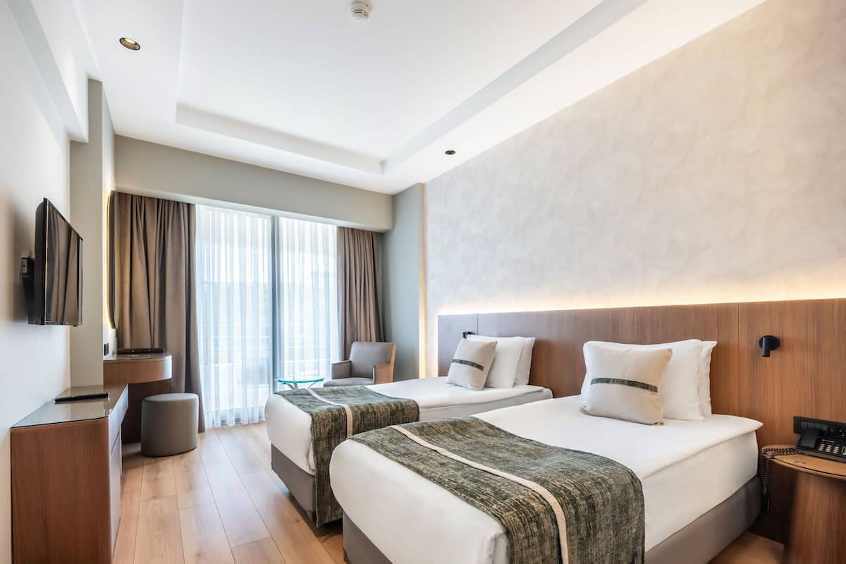 A hotel room with two beds, a TV, a desk, a chair, and a window with curtains.