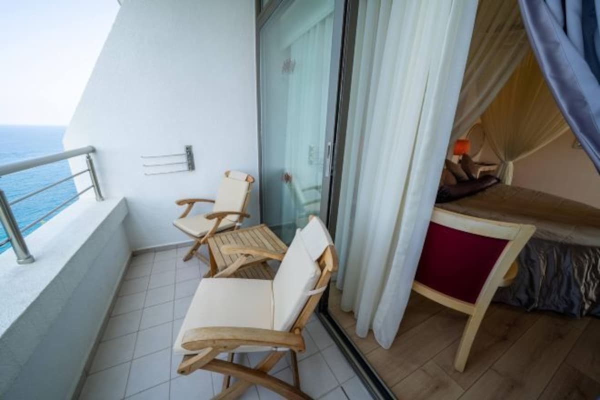 Un balcón con una mesa y dos sillas, una cama con dosel y vista al mar.