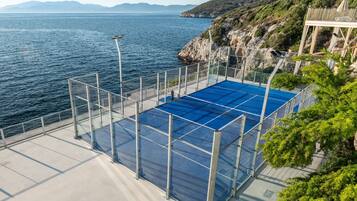 A blue pool with a metal fence, a white deck, and a view of the sea and hills.