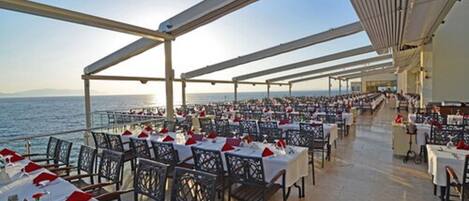 An outdoor dining area with tables and chairs, overlooking the sea.