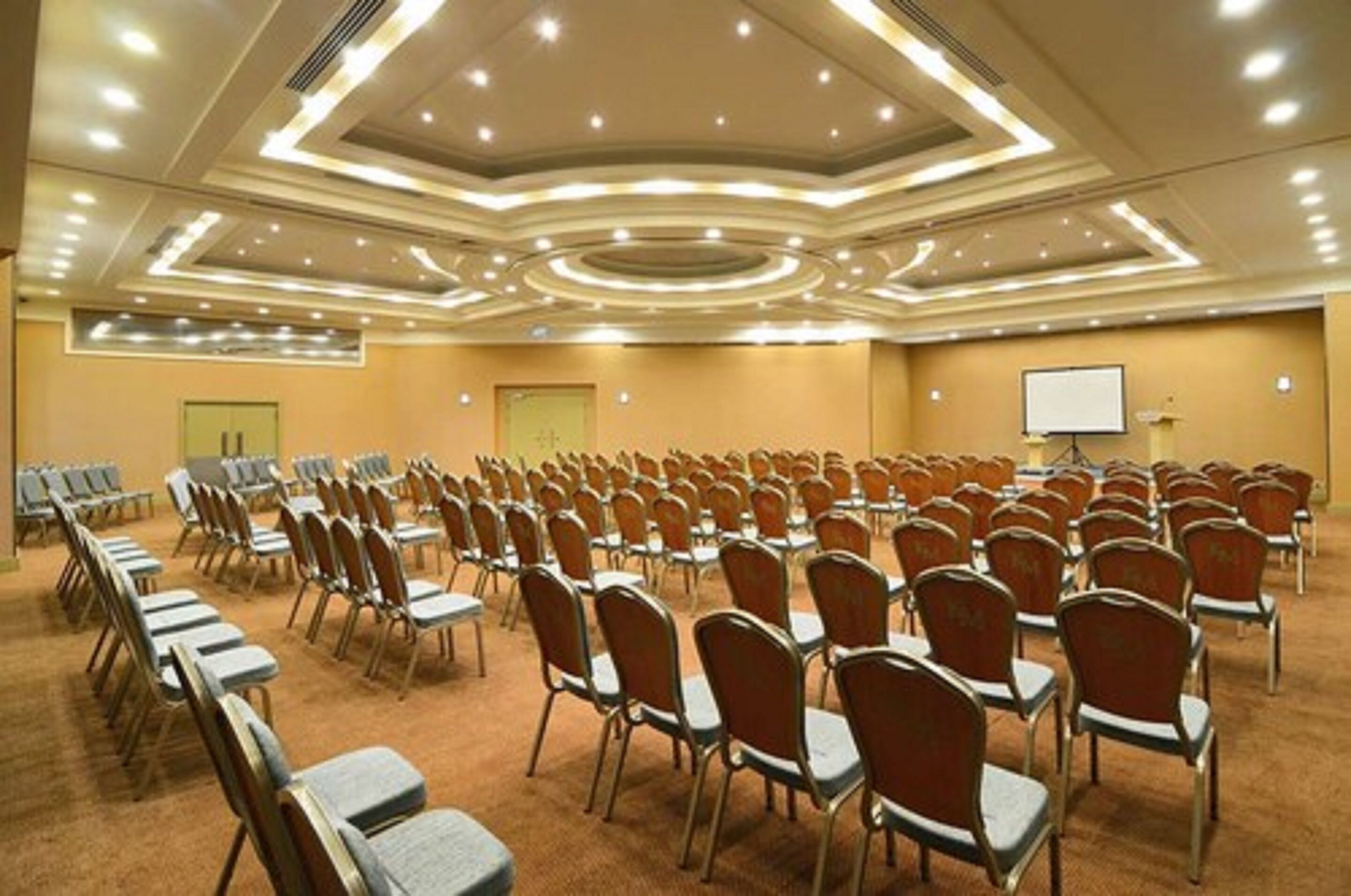 Une salle de conférence avec des rangées de chaises, un tableau blanc et un écran de projection.