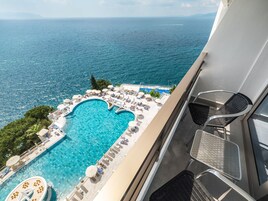Una piscina con diseño en forma de corazón, rodeada de sillones de descanso y sombrillas, con vista a una amplia extensión de agua.