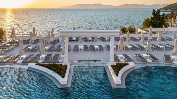 An aerial view of a resort with a pool, sun loungers, and umbrellas. - Korumar Deluxe Hotel (Kusadasi)