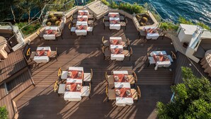 A deck with tables and chairs overlooking a body of water. - Korumar Deluxe Hotel (Kusadasi)