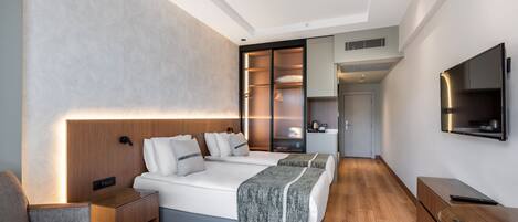 A modern hotel room with a large bed, a glass table, a sofa, a wardrobe, and a TV.