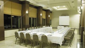 A conference room with long tables, chairs, a projector screen, and a whiteboard.