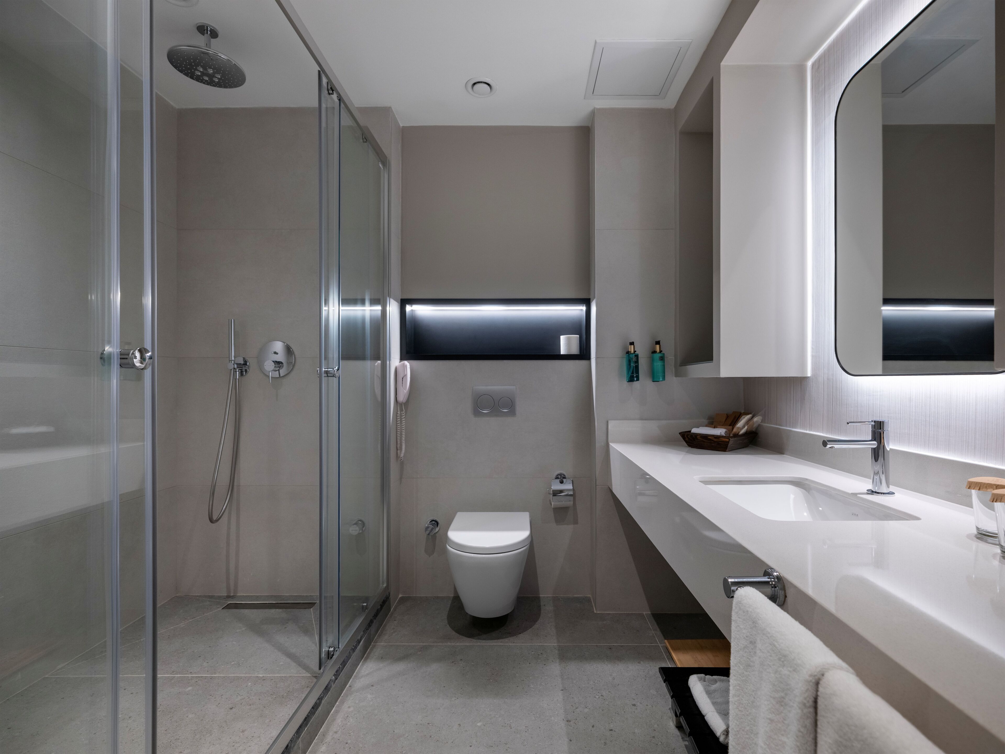 A modern bathroom with a glass-enclosed shower, a toilet, and a vanity with a large mirror.
