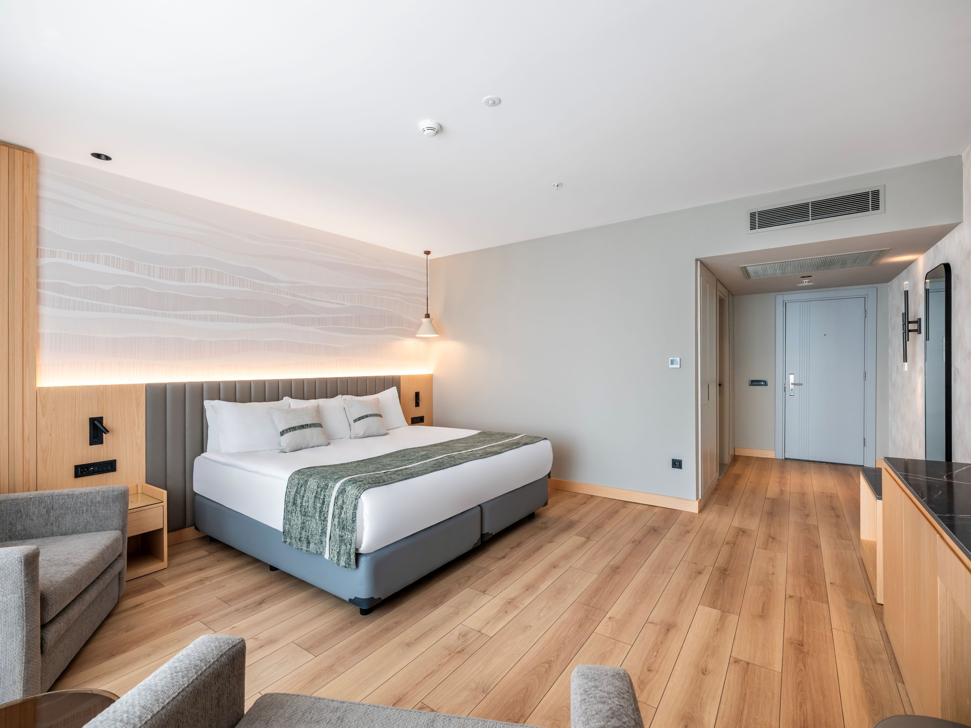 Une chambre d’hôtel moderne avec un grand lit, une table de chevet, une chaise et un luminaire fixé au mur.