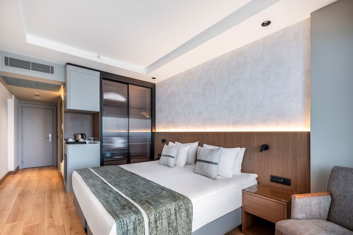 A modern hotel room with a large bed, a wooden nightstand, a glass coffee table, and a seating area.