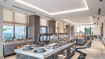 Una moderna presentación de buffet con múltiples estaciones de servicio, una encimera de mármol y vistas a la ciudad a través de grandes ventanales.