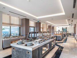 Una moderna presentación de buffet con múltiples estaciones de servicio, una encimera de mármol y vistas a la ciudad a través de grandes ventanales.