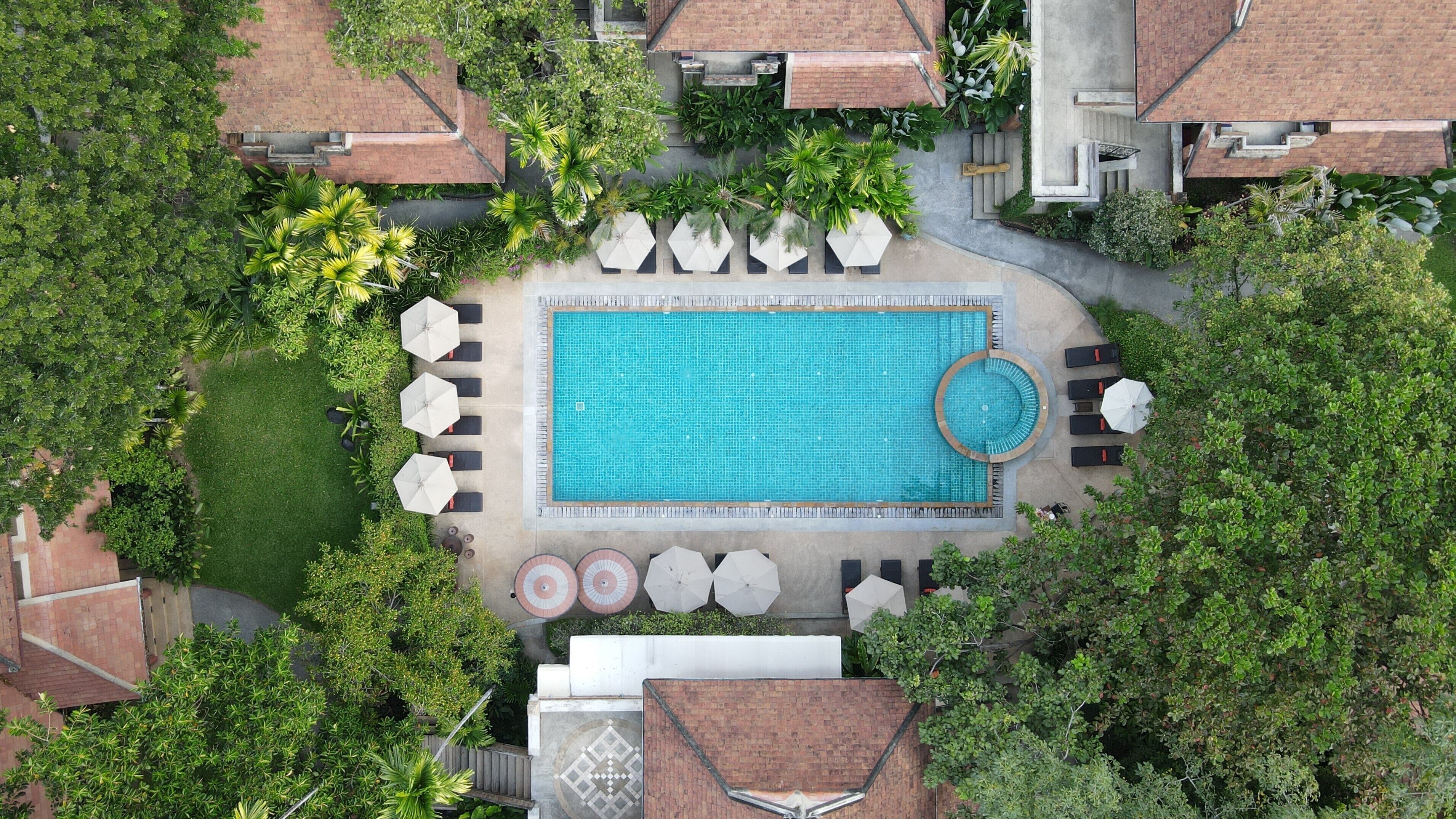 Une vue aérienne d’une piscine entourée de chaises longues et de parasols, avec un espace circulaire aménagé en jacuzzi.