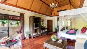 A spacious room with a wooden ceiling, a bed with a canopy, a television, a dining area with a table and chairs, and a kitchen area.