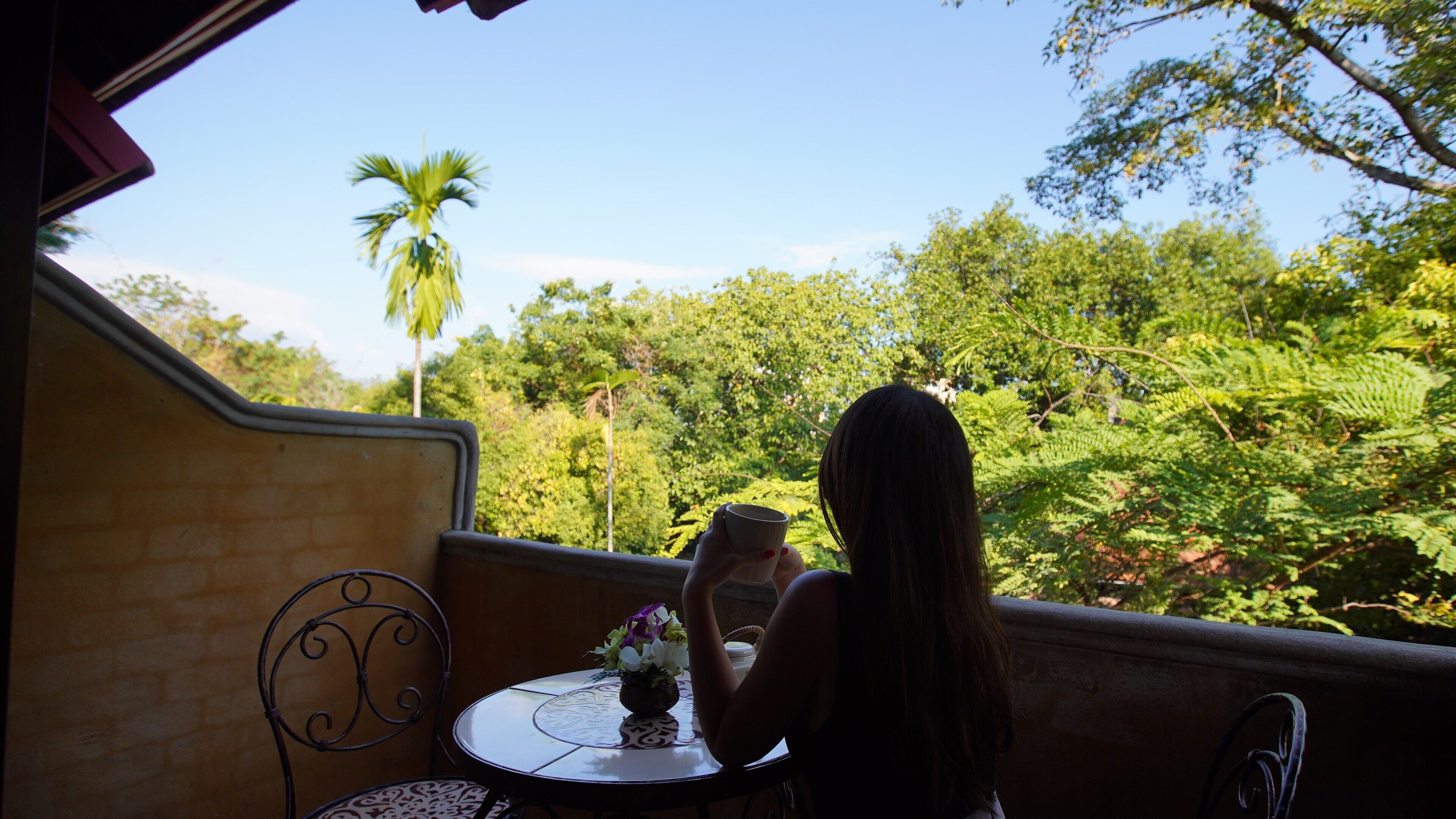 Una mujer sentada a una mesa con vista a un jardín exuberante.