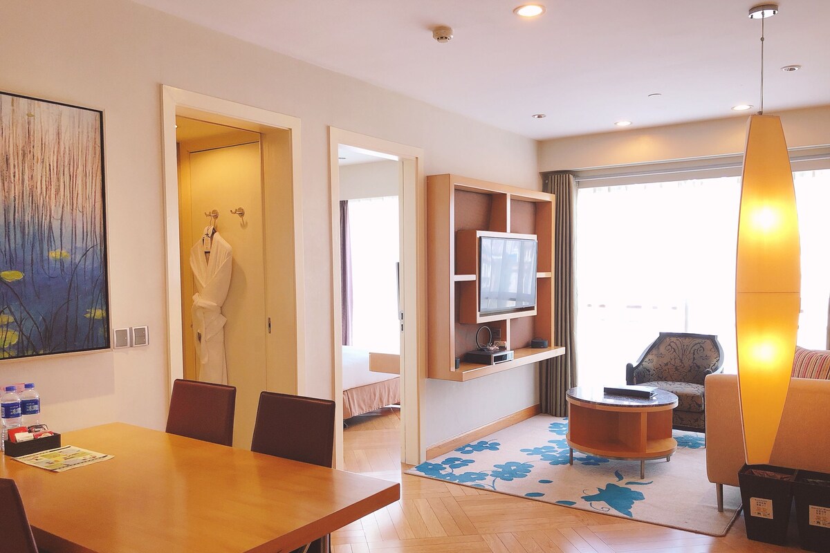 A hotel room with a dining area, a TV, a sofa, and a large window.