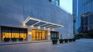 A modern hotel entrance with a glass facade, a sign reading "ASCOTT GUANGZHOU," and a covered outdoor area with potted plants. - Ascott Guangzhou (Guangzhou)
