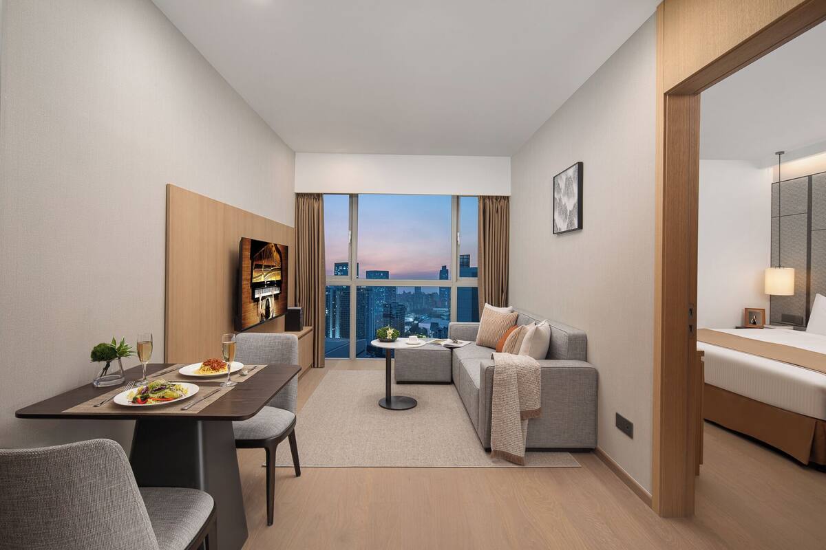 A modern hotel room with a dining area, a sofa, a bed, and a city view.