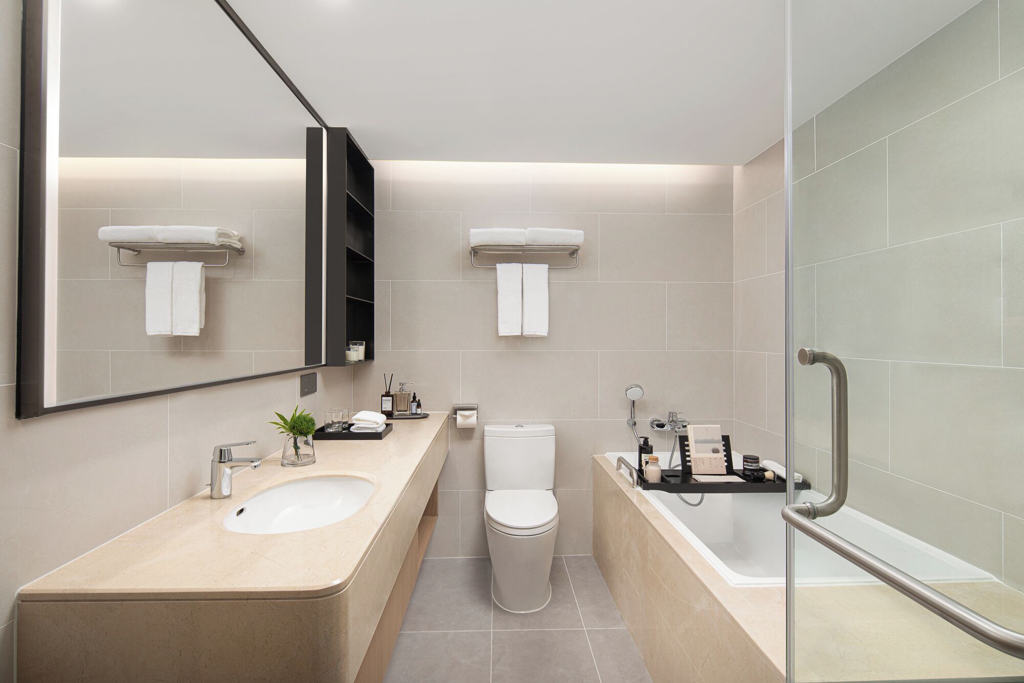 A modern bathroom with a large mirror, two sinks, a toilet, and a bathtub.