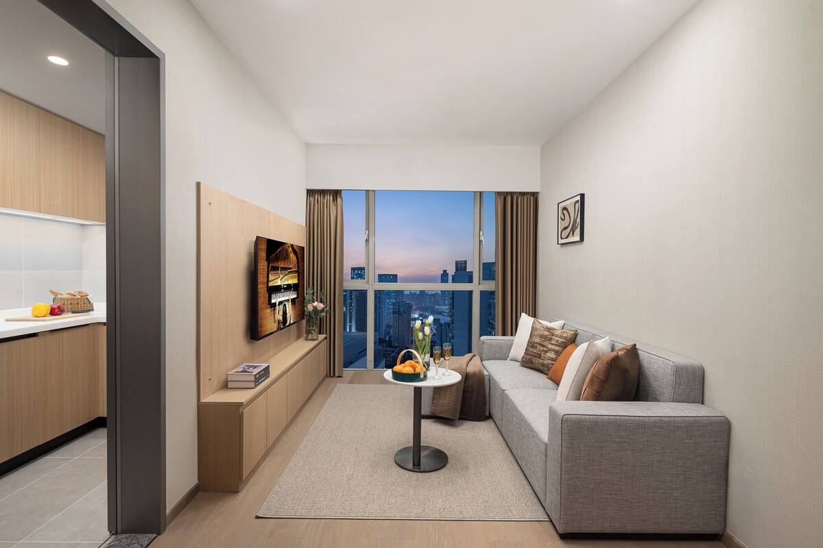 A modern living room with a grey sofa, a small round table, and a city view through large windows.