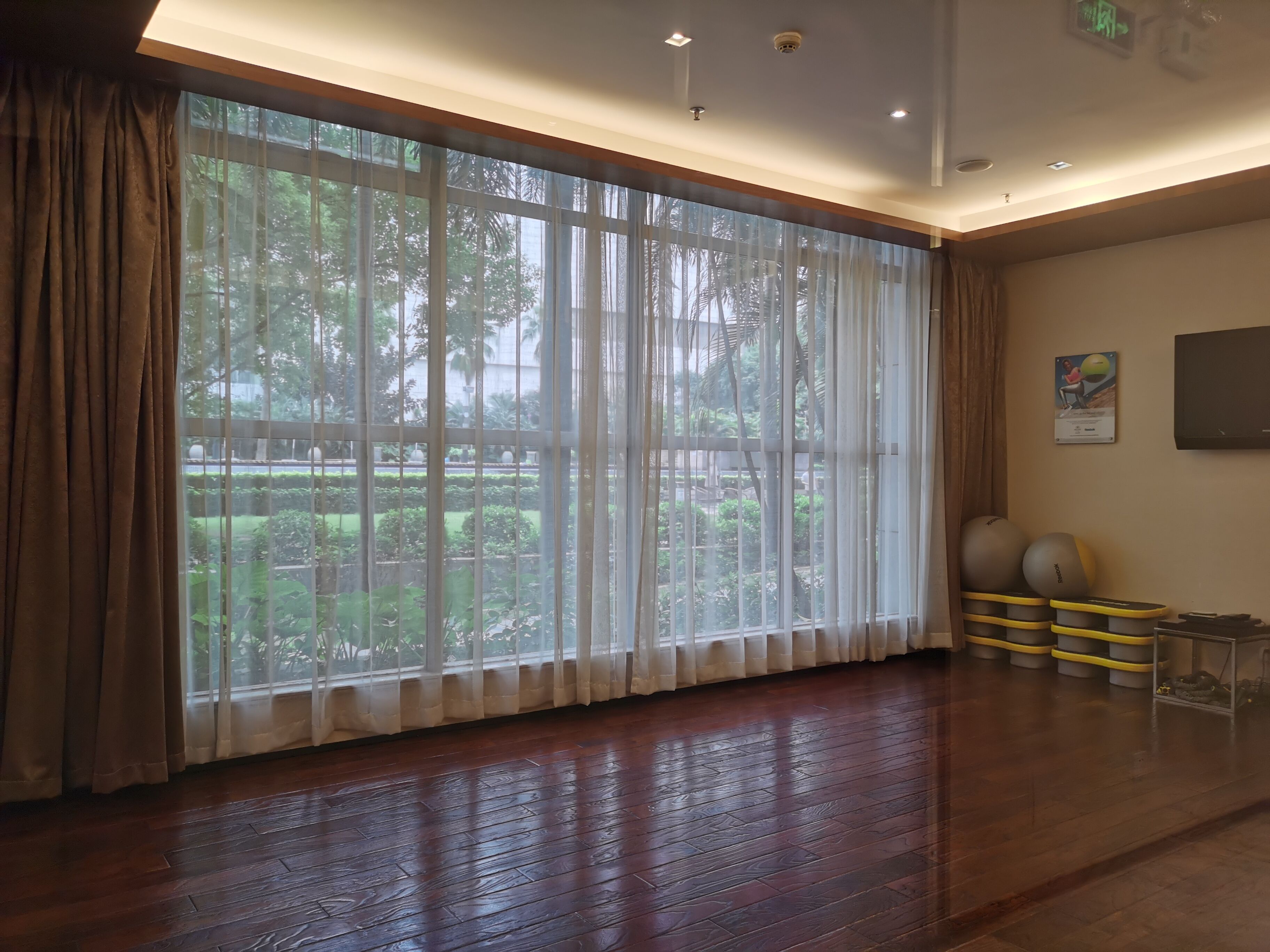 A spacious room with large windows, wooden flooring, and exercise equipment.