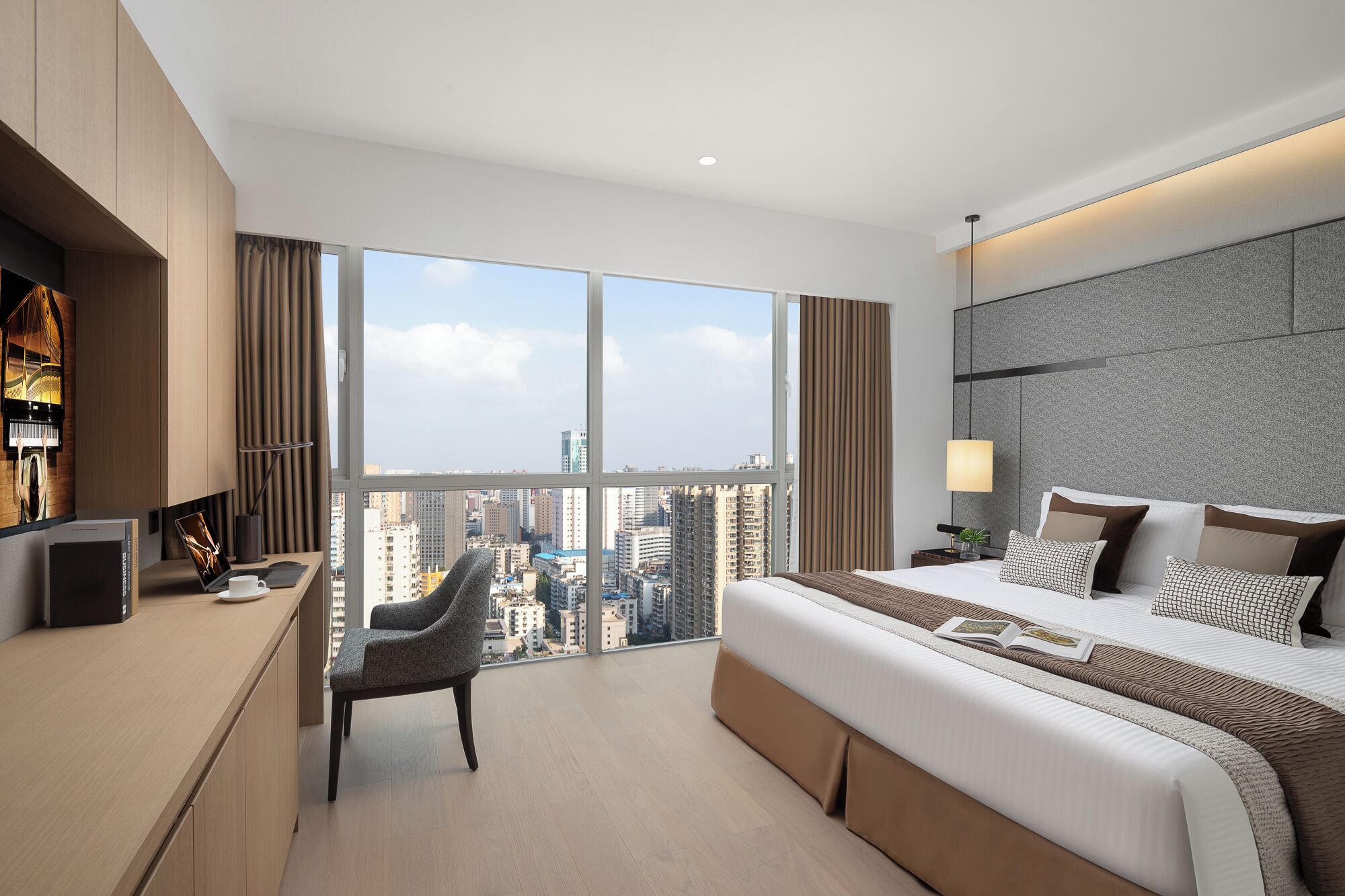 Une chambre d’hôtel moderne dotée d’un grand lit, d’un bureau, d’une chaise et offrant une vue sur la ville grâce à de grandes fenêtres.