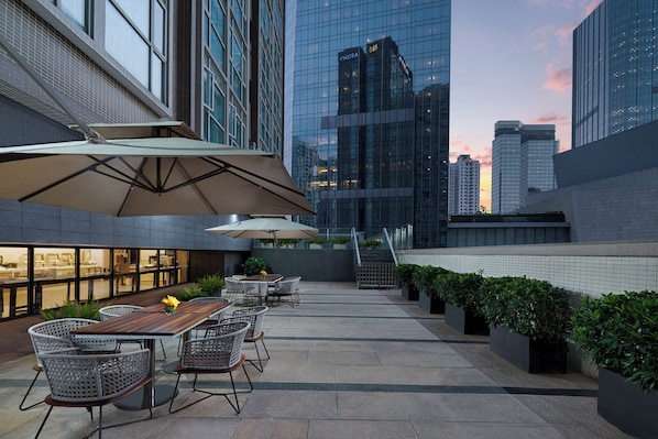 Un espacio exterior con mesas y sillas para comer, una escalera y vistas a edificios modernos.