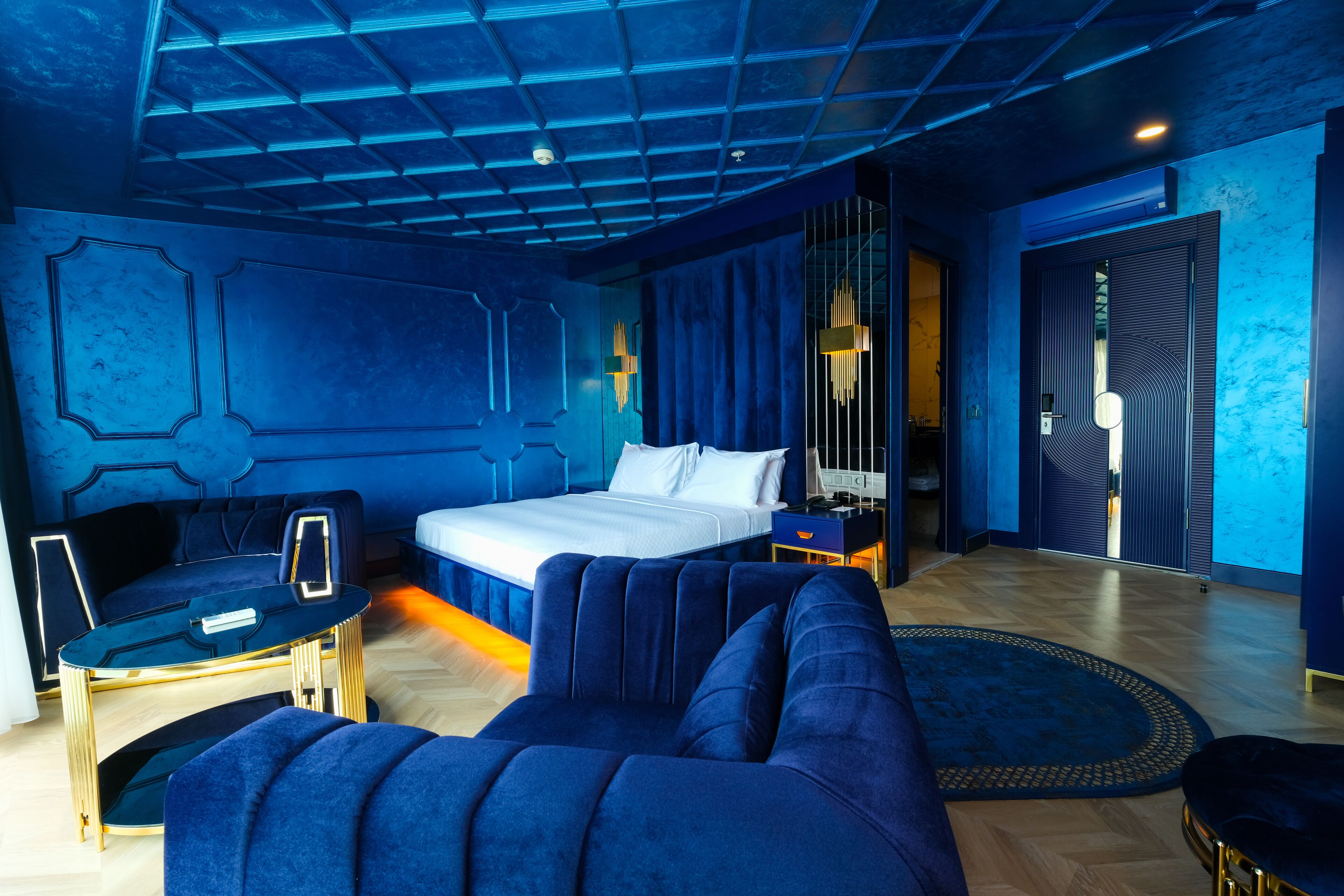 Ein modernes Hotelzimmer mit einem großen Bett, einem blauen Sofa, einem kleinen Tisch und einem dekorativen Teppich.