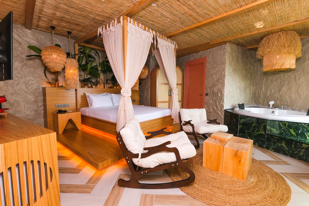 Un dormitorio con una cama, un escritorio de madera, un sillón mecedor, un baño con bañera y un espejo grande.