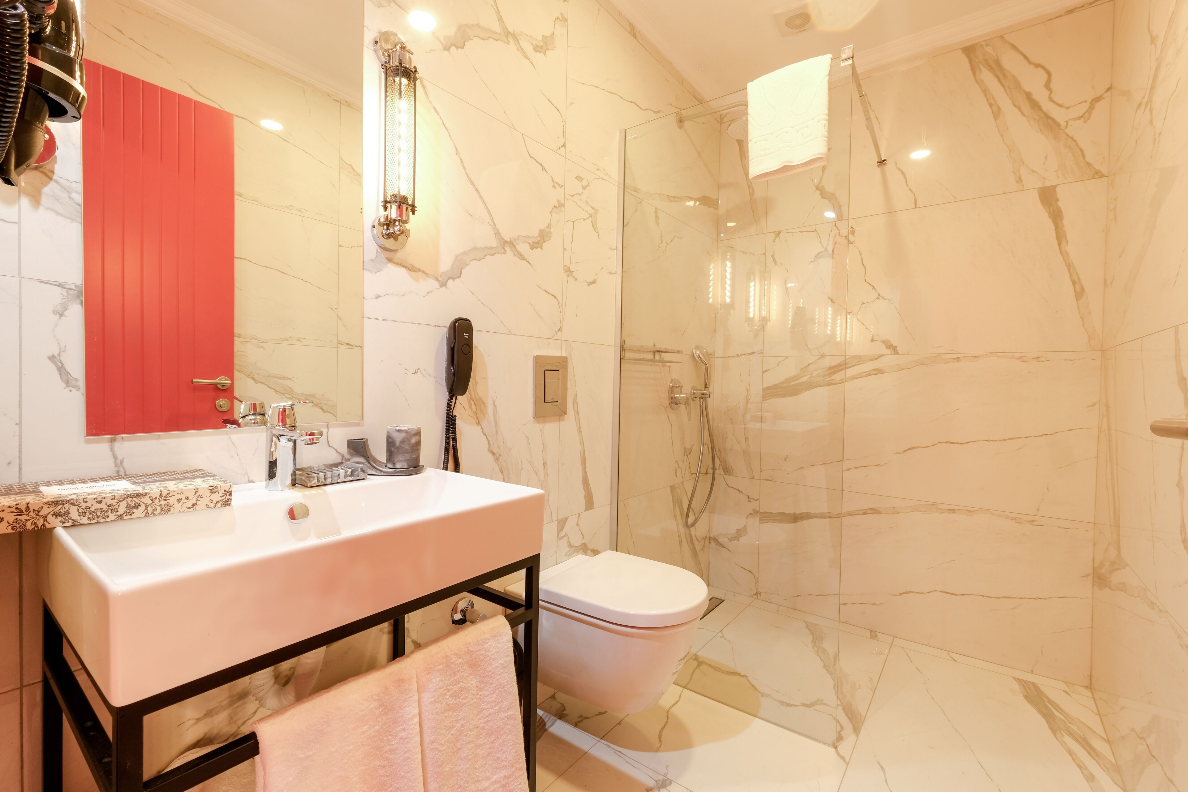 Ein modernes Badezimmer mit Marmorwand, Waschbecken in Weiß, Toilette und einer Duschkabine aus Glas.