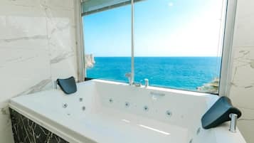 Un baño con una bañera amplia, vistas al océano y paredes de mármol.