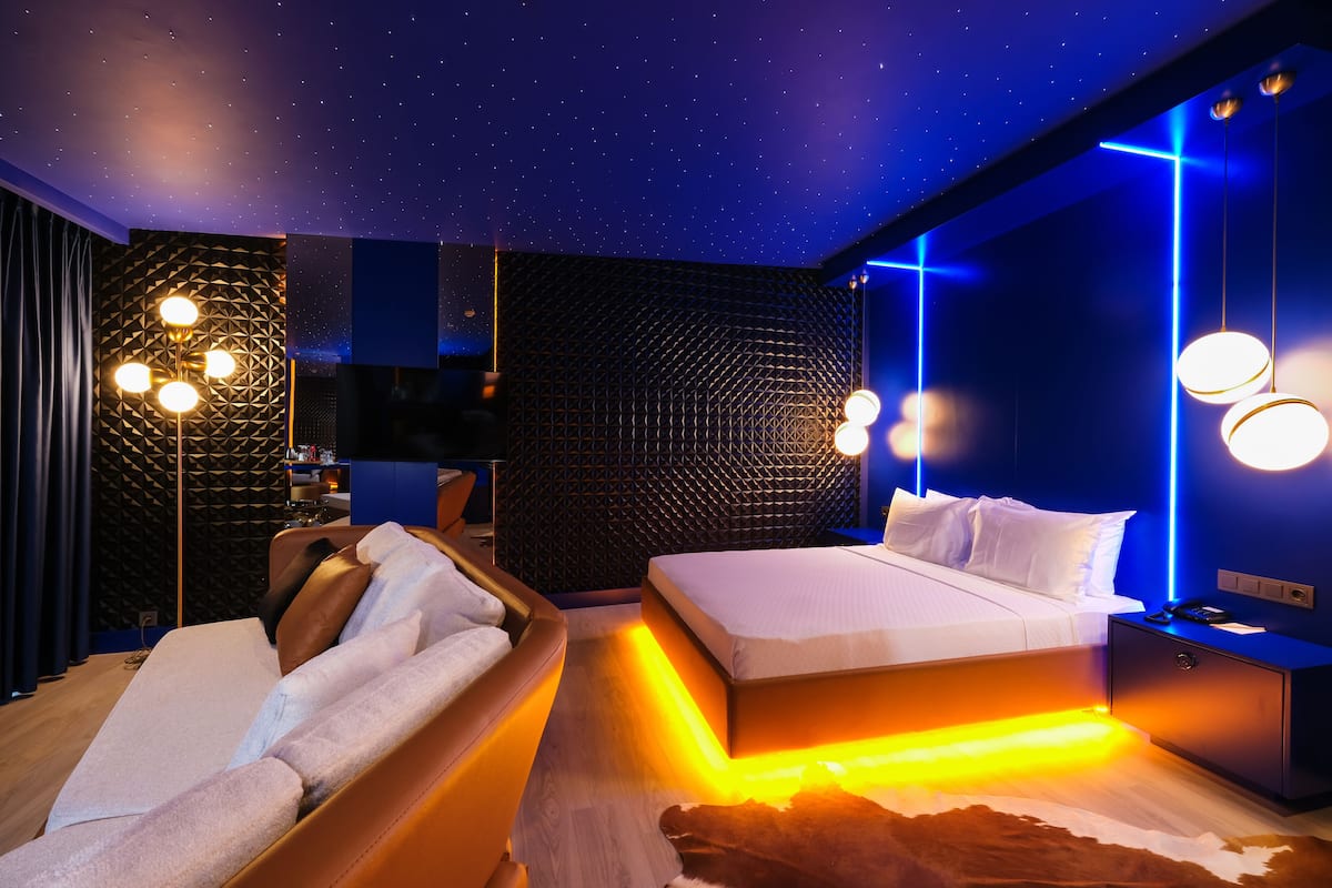 Un dormitorio moderno con techo estrellado, una cama, un sofá y una mesita de noche.