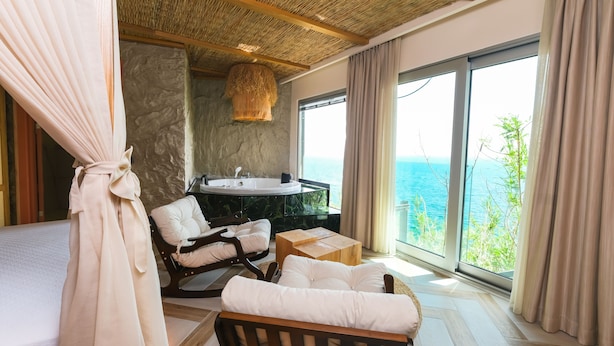 Un dormitorio con un ventanal grande, una bañera y una silla de madera.