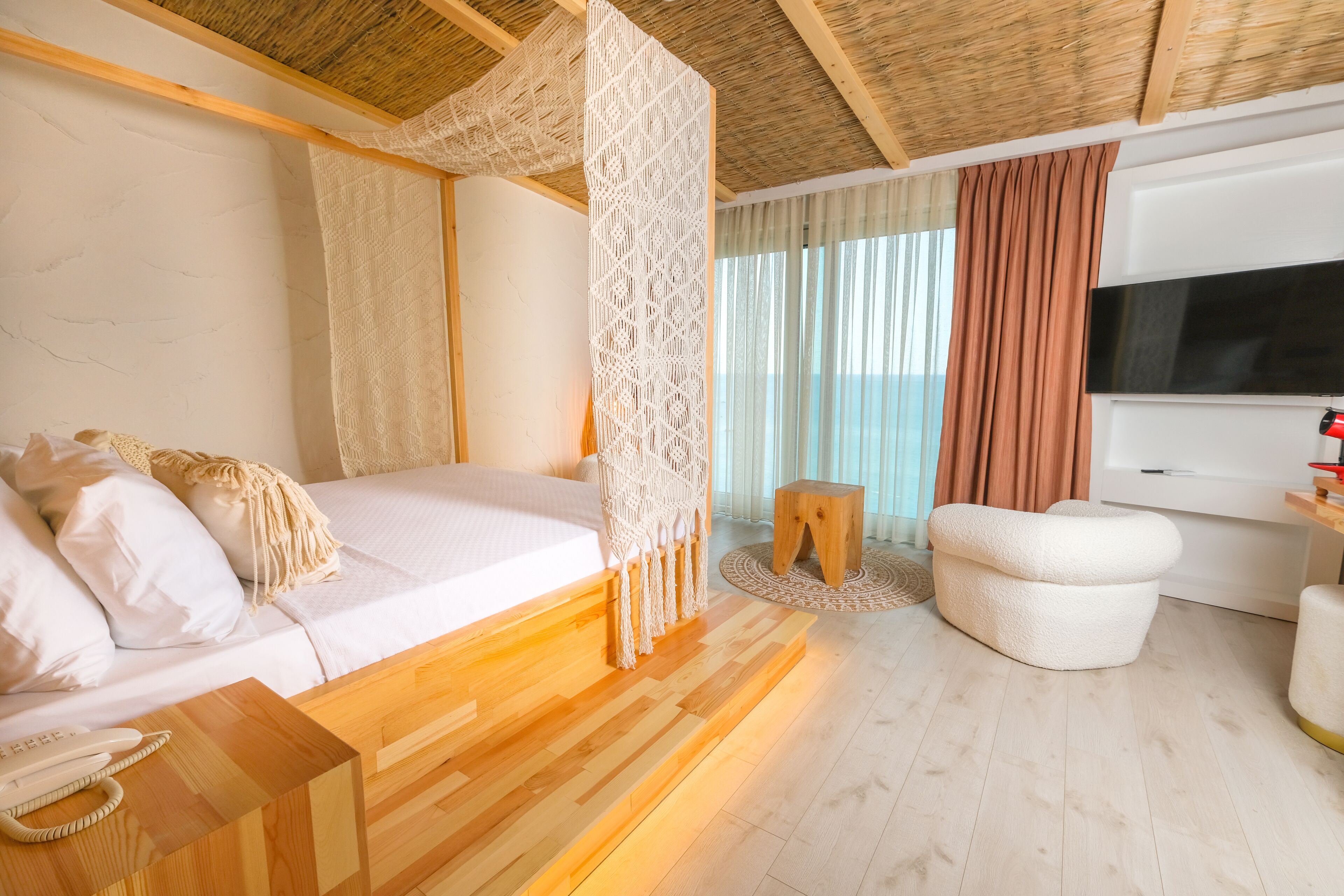 A modern bedroom with a wooden bed, a TV, and a small wooden stool.
