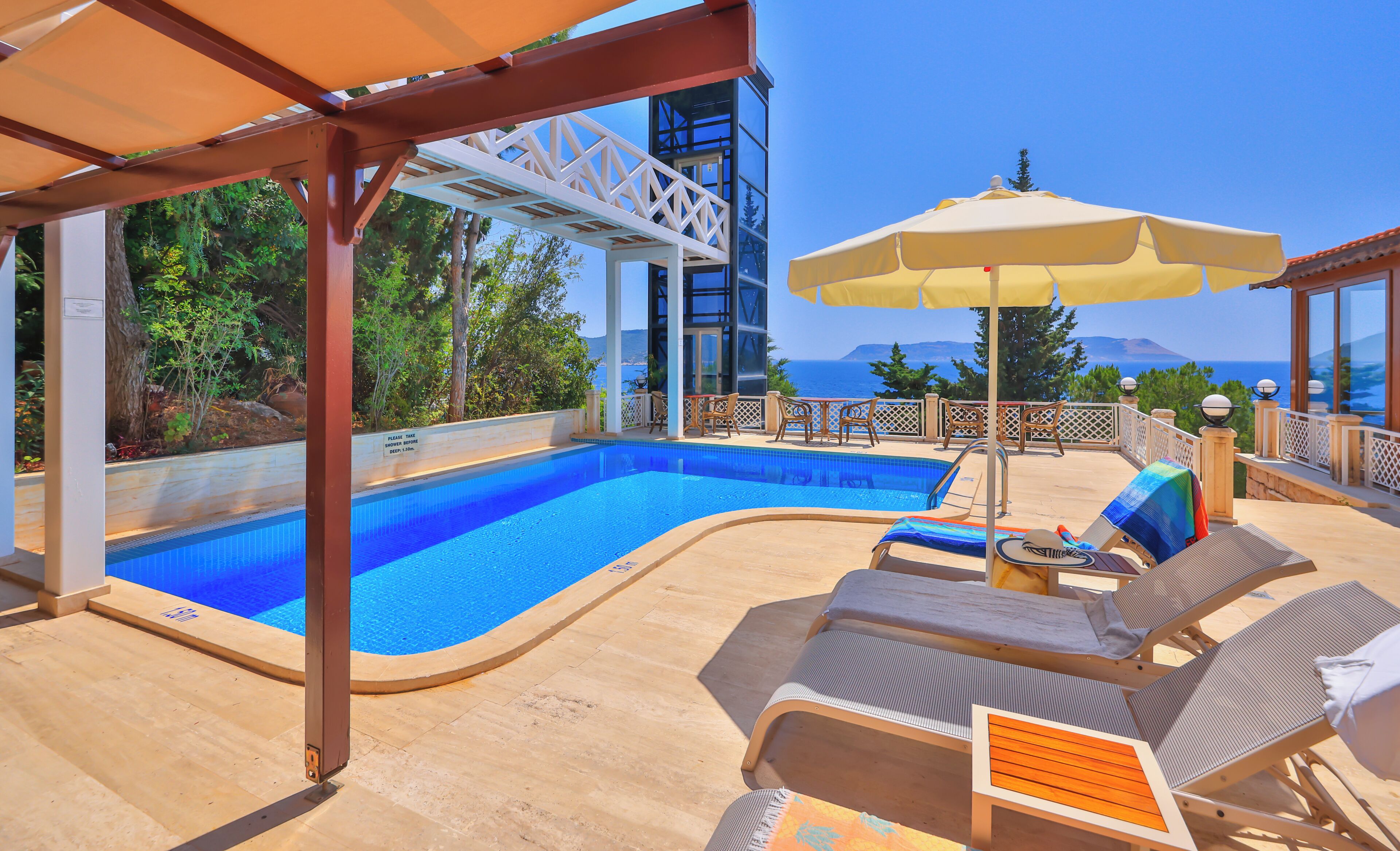 Zona de piscina con sillas de descanso y una sombrilla, rodeada por una terraza de madera y con vistas a un paisaje idílico.