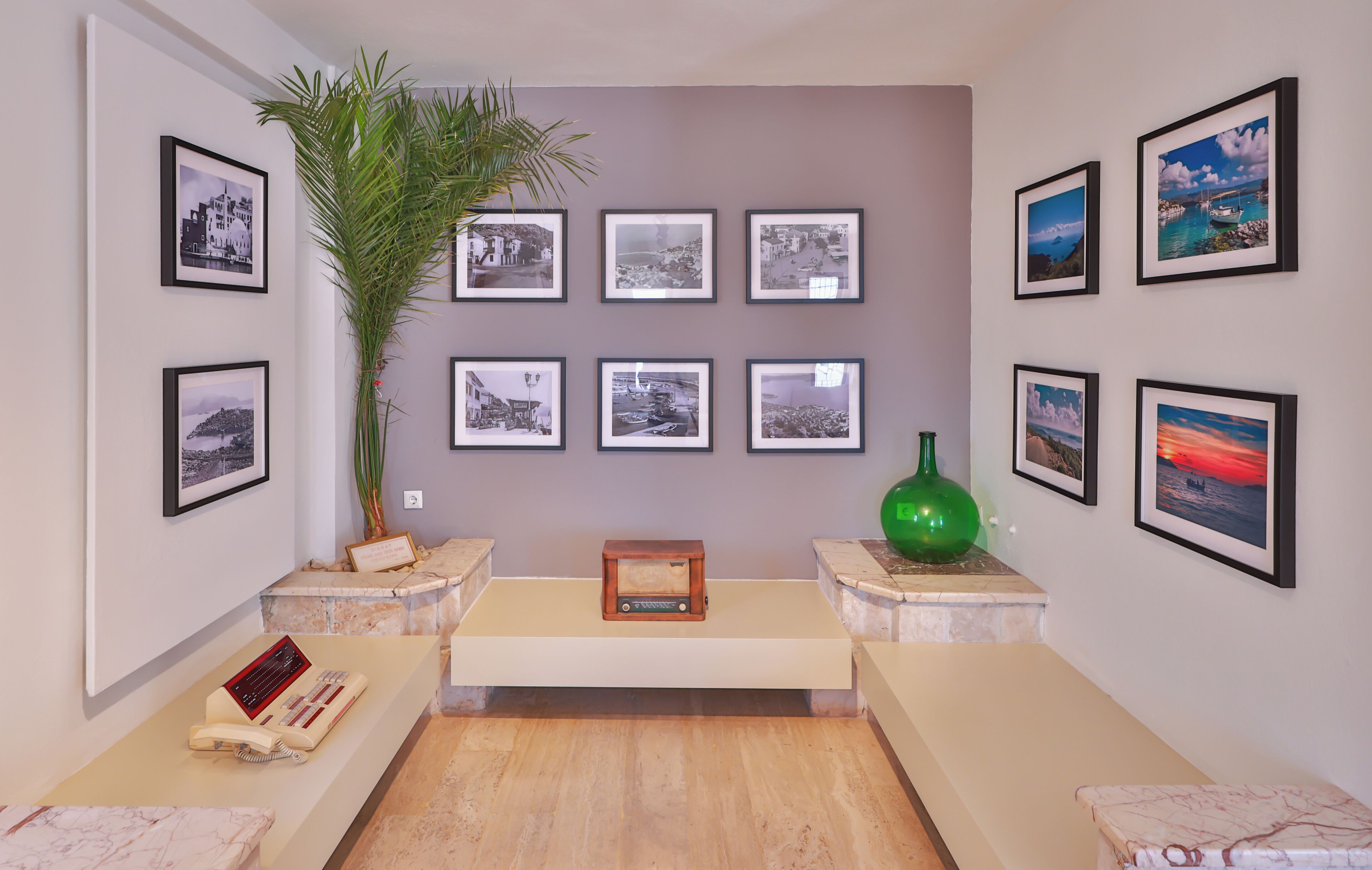 A room with a marble floor, a large potted plant, a small wooden radio, and framed photographs on the walls.
