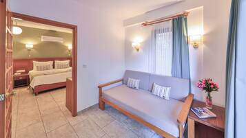 A hotel room with a bed, a sofa, a nightstand, a lamp, and a window with curtains.