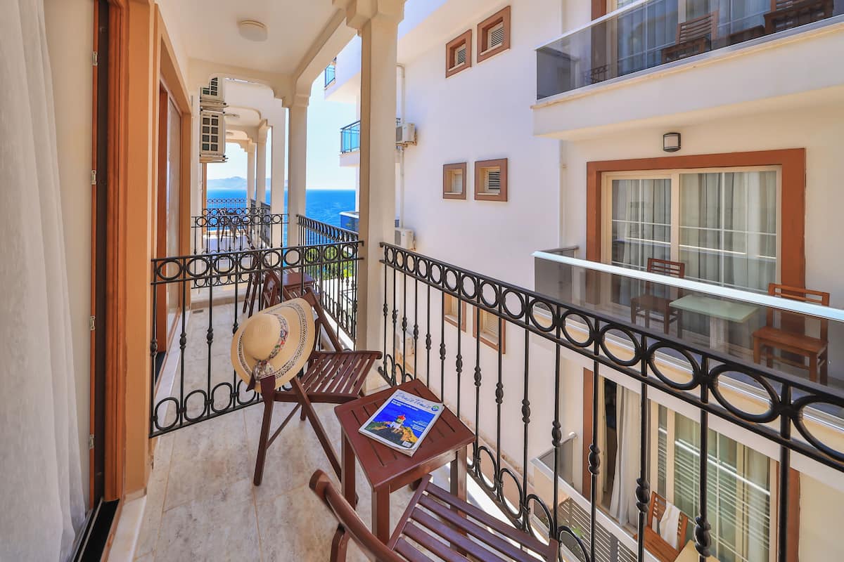 A balcony with a wooden chair, a small table with a magazine, and a view of the sea.