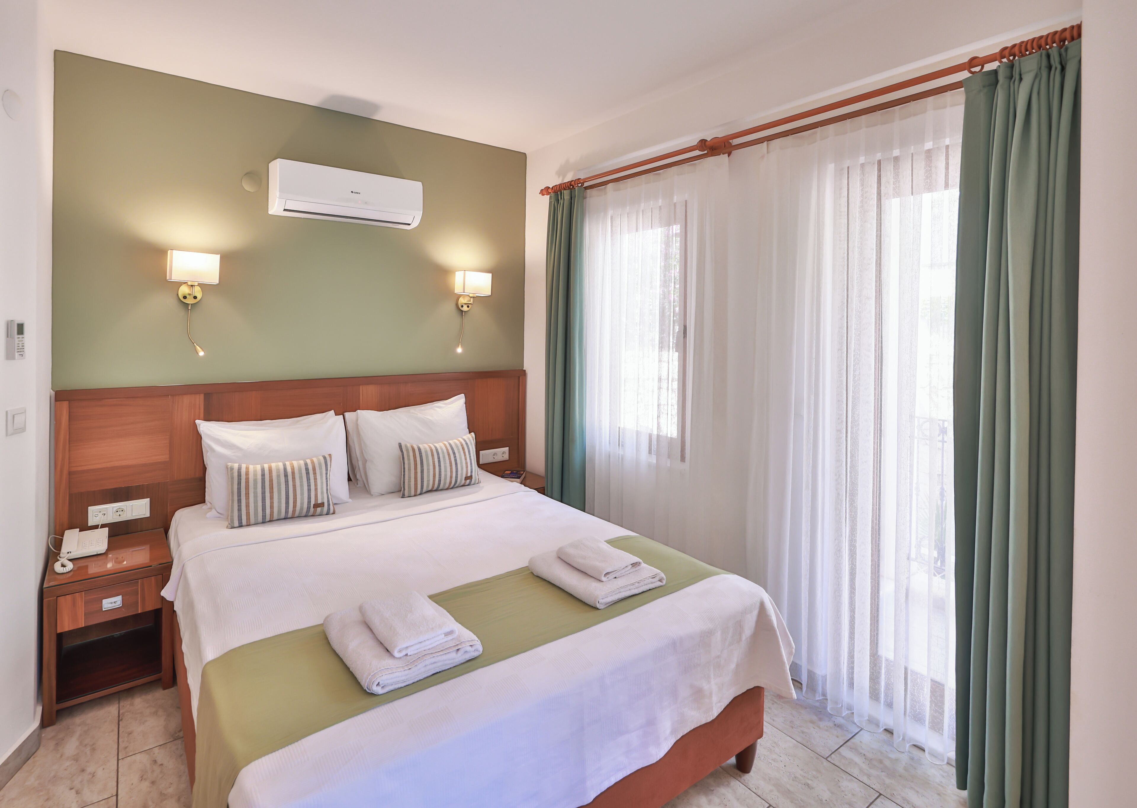 A hotel room with a bed, bedside lamps, a phone, a nightstand, and a window with curtains.