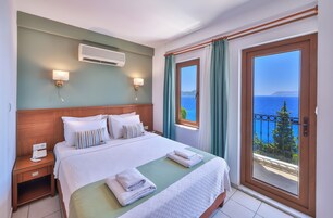 A hotel room with a bed, bedside lamps, an air conditioner, a view of the sea, and a balcony with a railing.