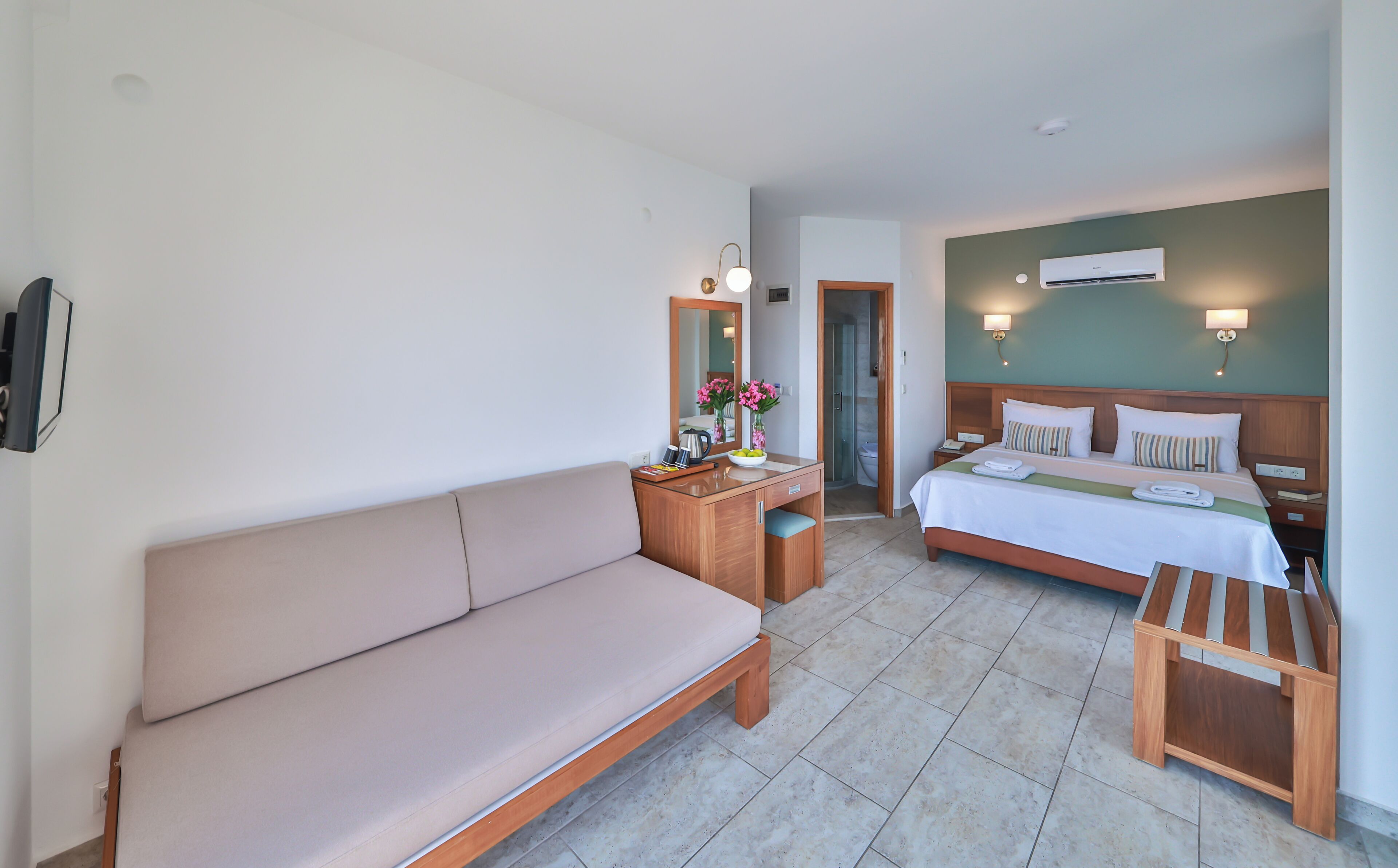 Una habitación de hotel con una cama, un sofá, un escritorio con espejo, una mesita de noche y un equipo de aire acondicionado.