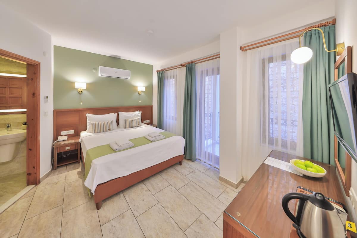 A hotel room with a bed, bedside table, kettle, and a view of the outdoors.