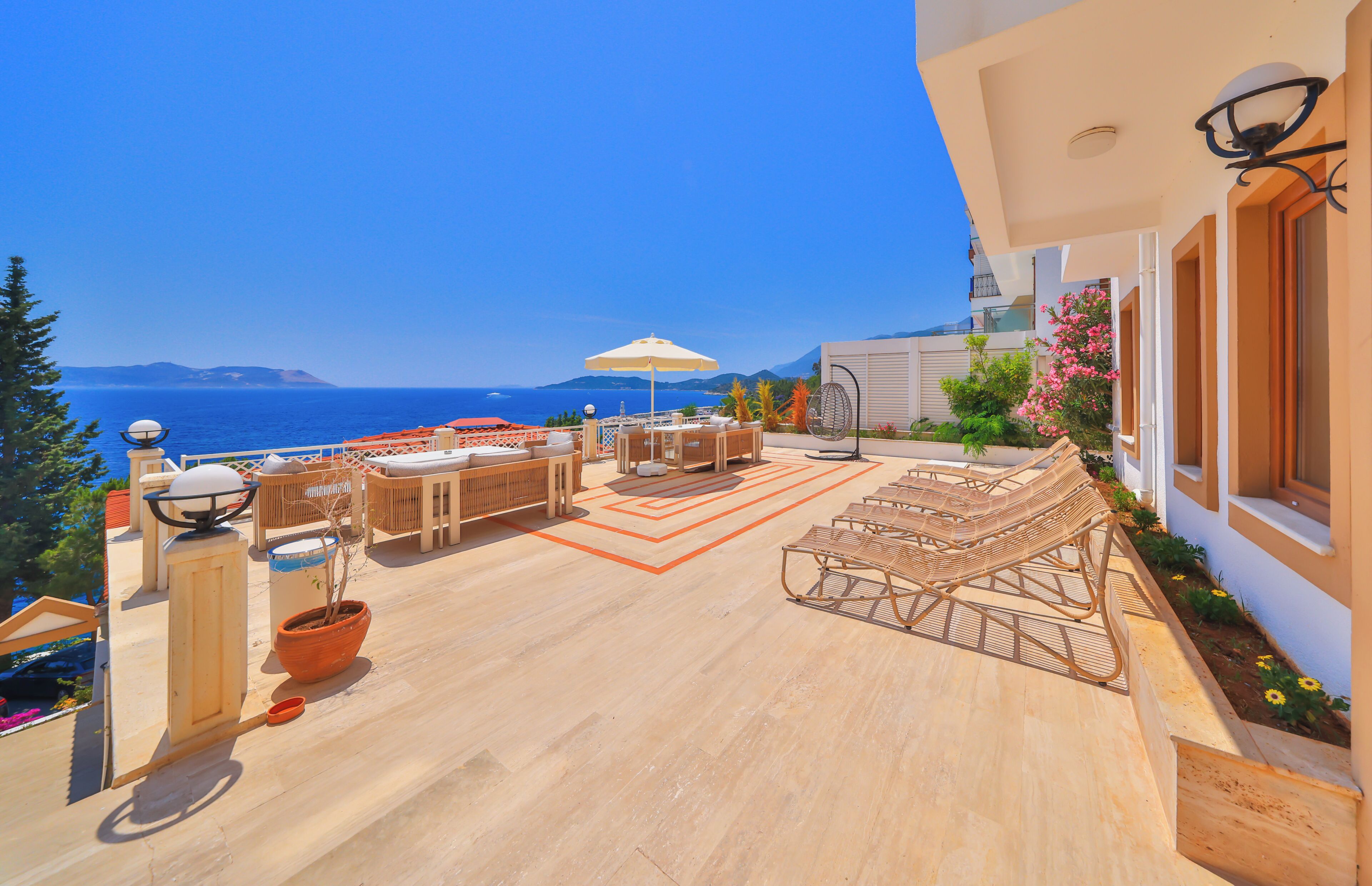 A sunlit terrace with outdoor furniture, a potted plant, and a view of the sea.
