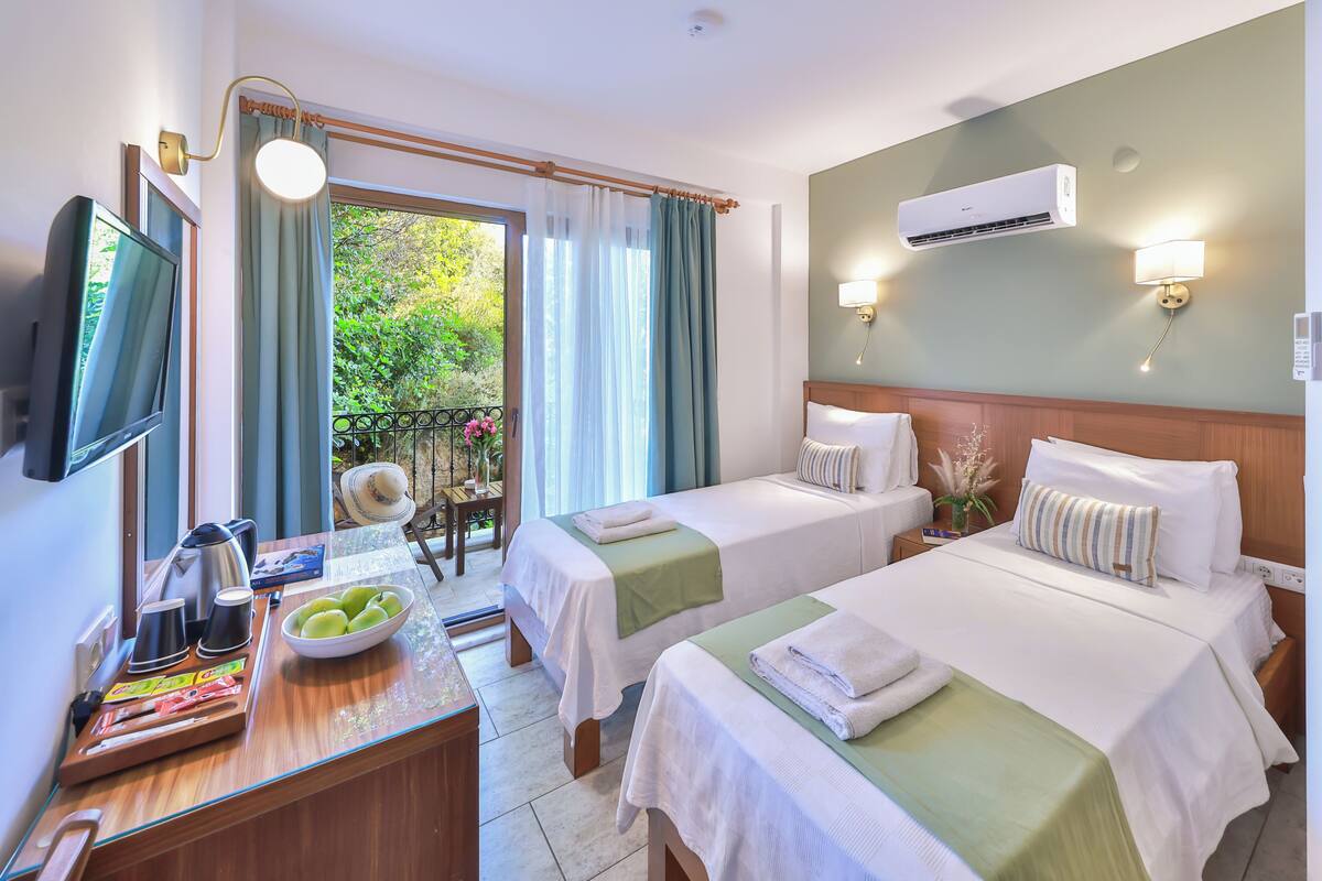 A hotel room with two beds, a TV, a desk with a bowl of fruit, and an air conditioning unit.