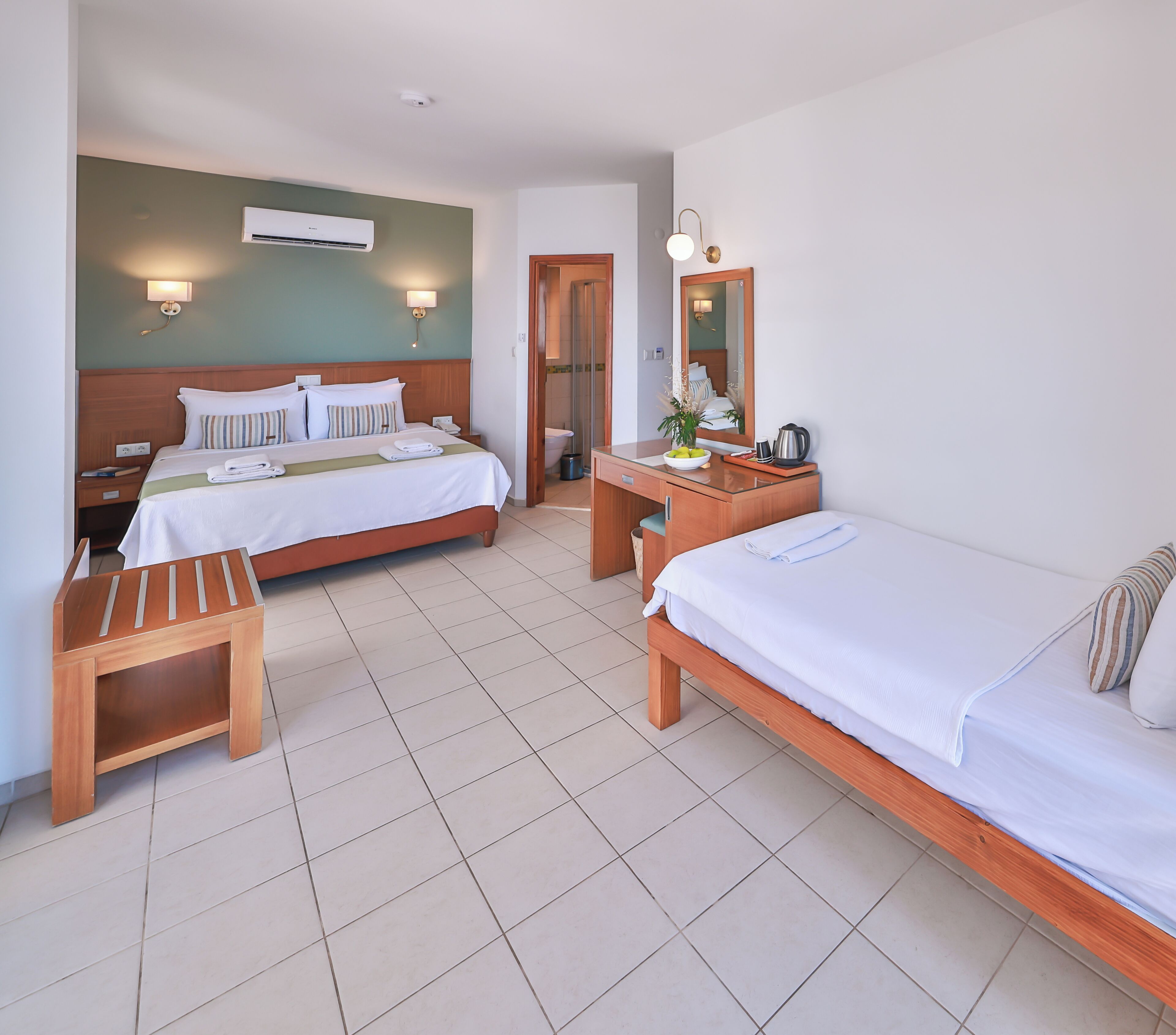 Een hotelkamer met twee bedden, een bureau, een stoel, een spiegel en een badkamer zichtbaar door een geopende deur.