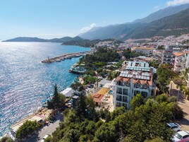 Un pueblo costero con edificios, un puerto deportivo y montañas al fondo.
